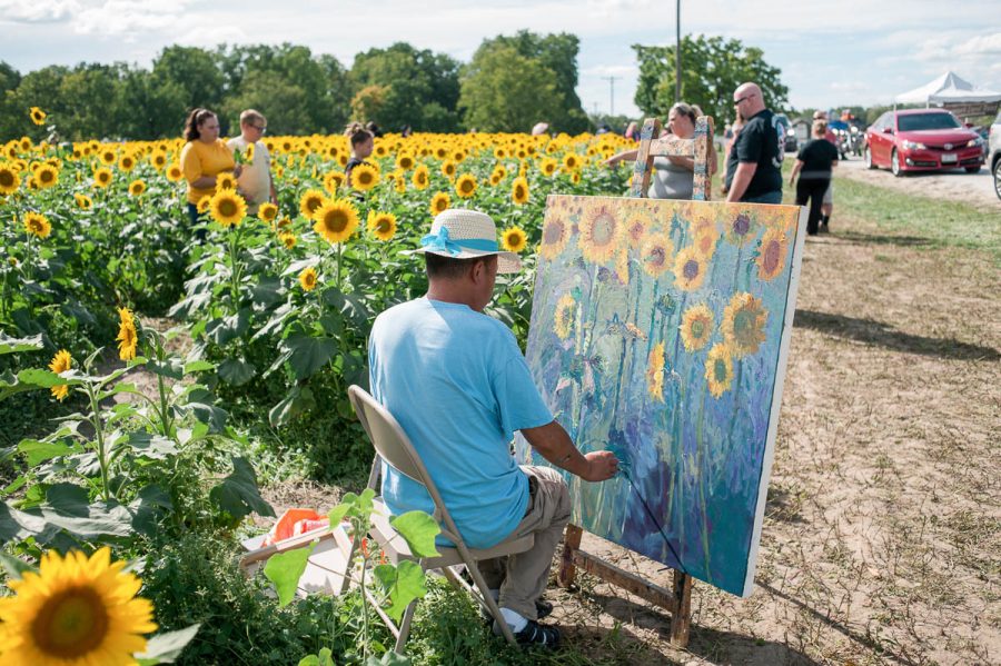 a man painting plein air next to a sunflower field
